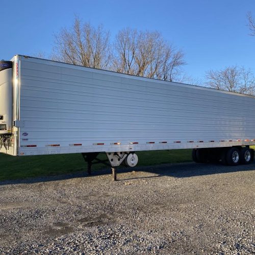 A white trailer parked on gravel road.